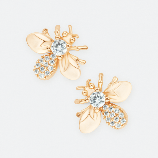 The Apis earrings by Ocarina, 18K gold-plated stud earrings shaped like bees, featuring sparkling zircon stones on the body and a large central gemstone. A nature-inspired jewelry piece symbolizing harmony and perseverance, displayed against a clean white background.