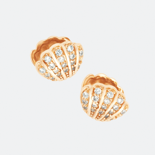 The Concha earrings by Ocarina, 18K gold-plated stud earrings in the shape of seashells, adorned with shimmering zircon stones. A luxurious ocean-inspired jewelry piece capturing the beauty of marine treasures, displayed against a clean white background.