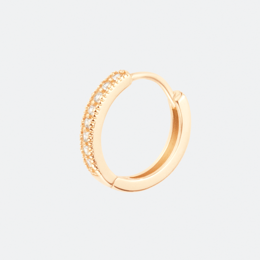 The Gloriosa hoop earring by Ocarina, an 18K gold-plated design encrusted with shimmering zircon stones. A delicate and timeless jewelry piece that adds elegance and sparkle, displayed against a clean white background with a subtle blue accent.