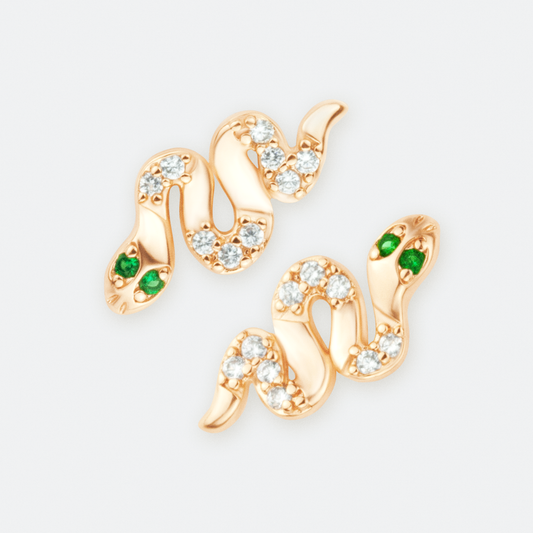 The Venefica earrings by Ocarina, 18K gold-plated snake-shaped stud earrings adorned with shimmering zircon stones and striking green gemstone eyes. A bold and mystical jewelry piece symbolizing transformation and power, displayed against a clean white background.